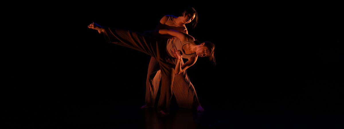 Two dancers perform against a black background.