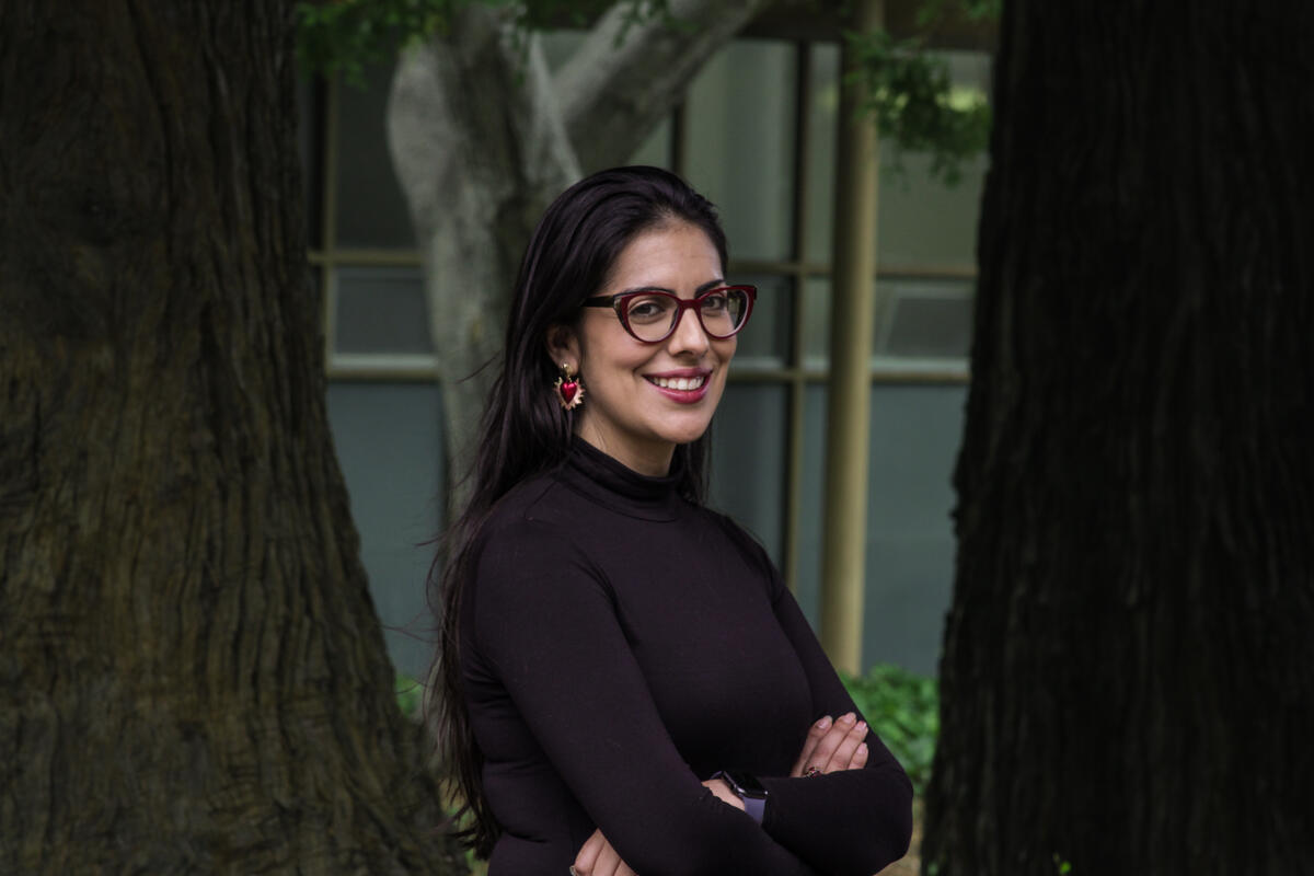 A headshot of Karina Gutiérrez, she is wearing red frame glasses, red earrings, and a black sweater.