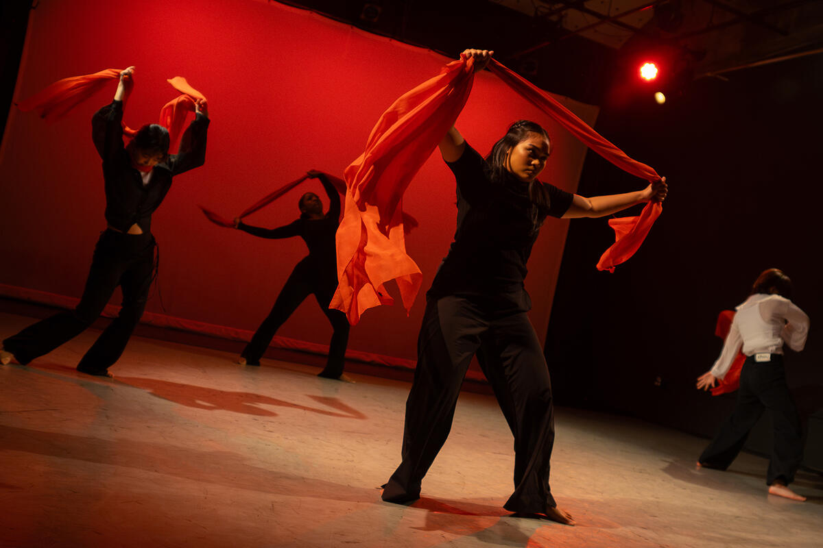 Four dancers perform with red scarves against a red backdrop